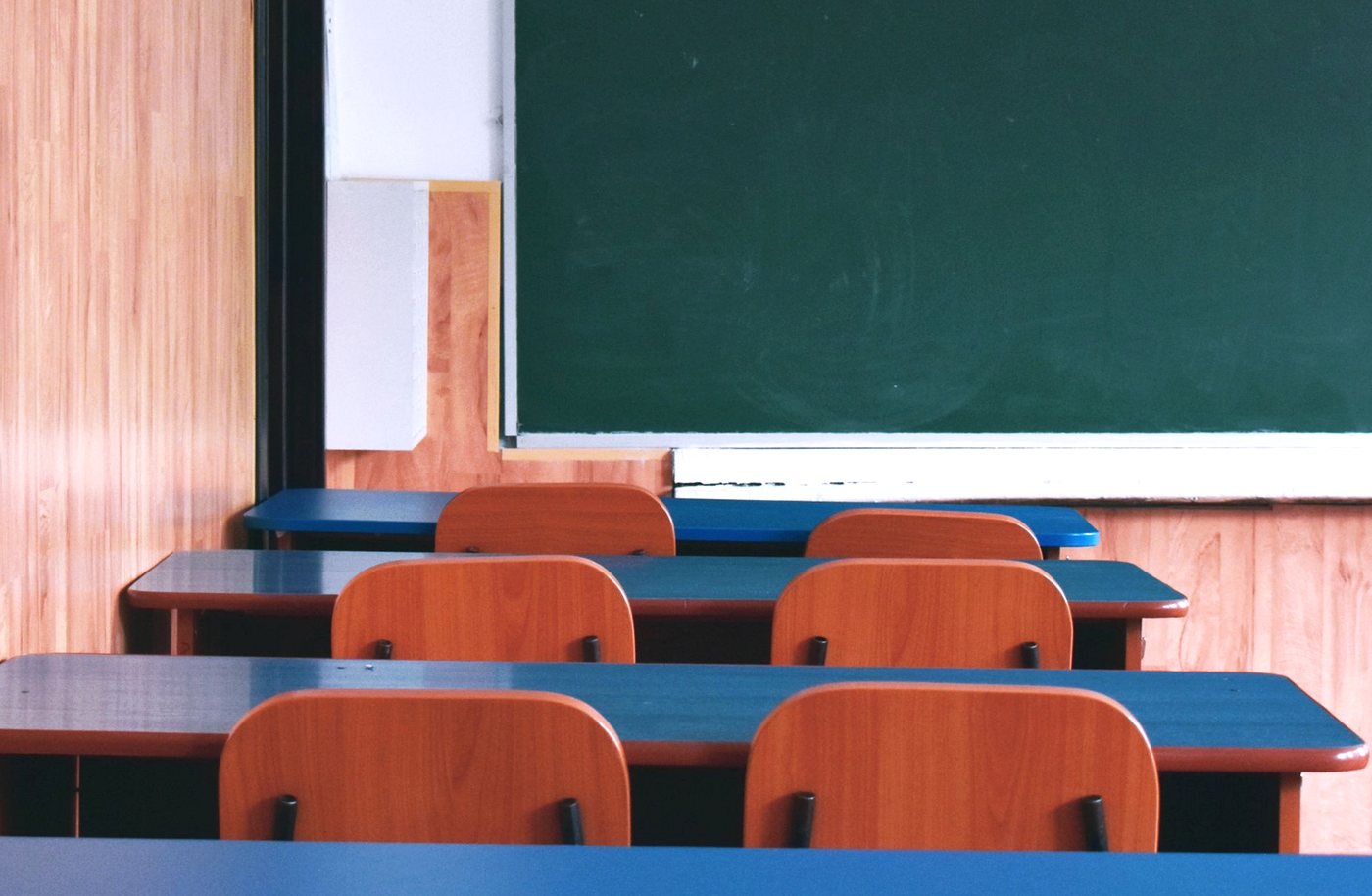 Empty classroom with wooden chairs, blue desks and a chalkboard